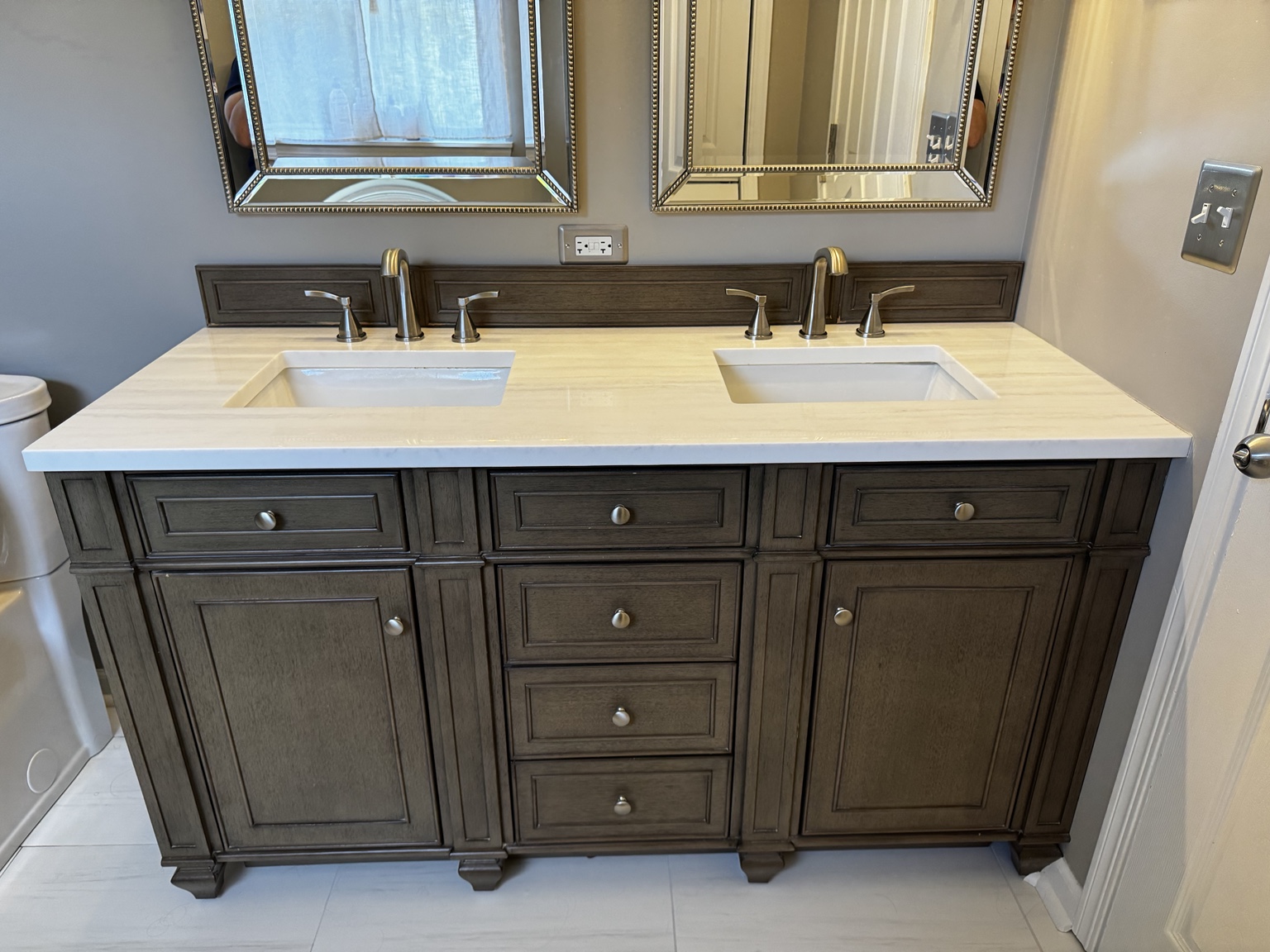 Walnut bathroom vanity with double sinks, pale countertop, framed mirrors, and brushed metal fixtures