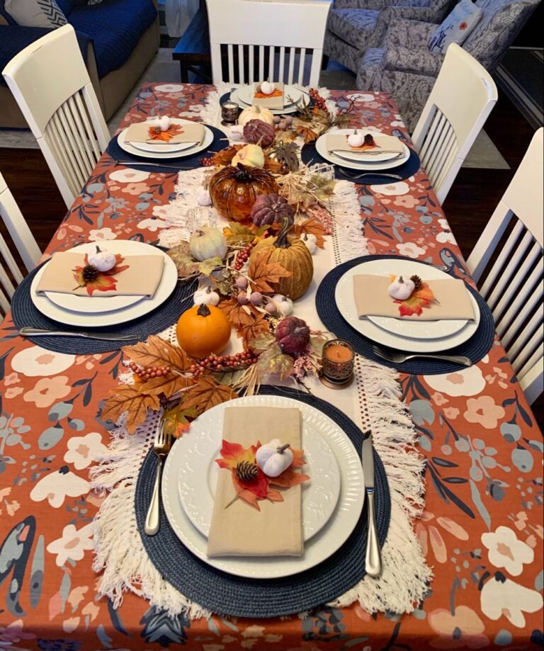 Thanksgiving dining table with a burnt-orange floral tablecloth, navy placemats, ivory plates and an autumn pumpkin centerpiece