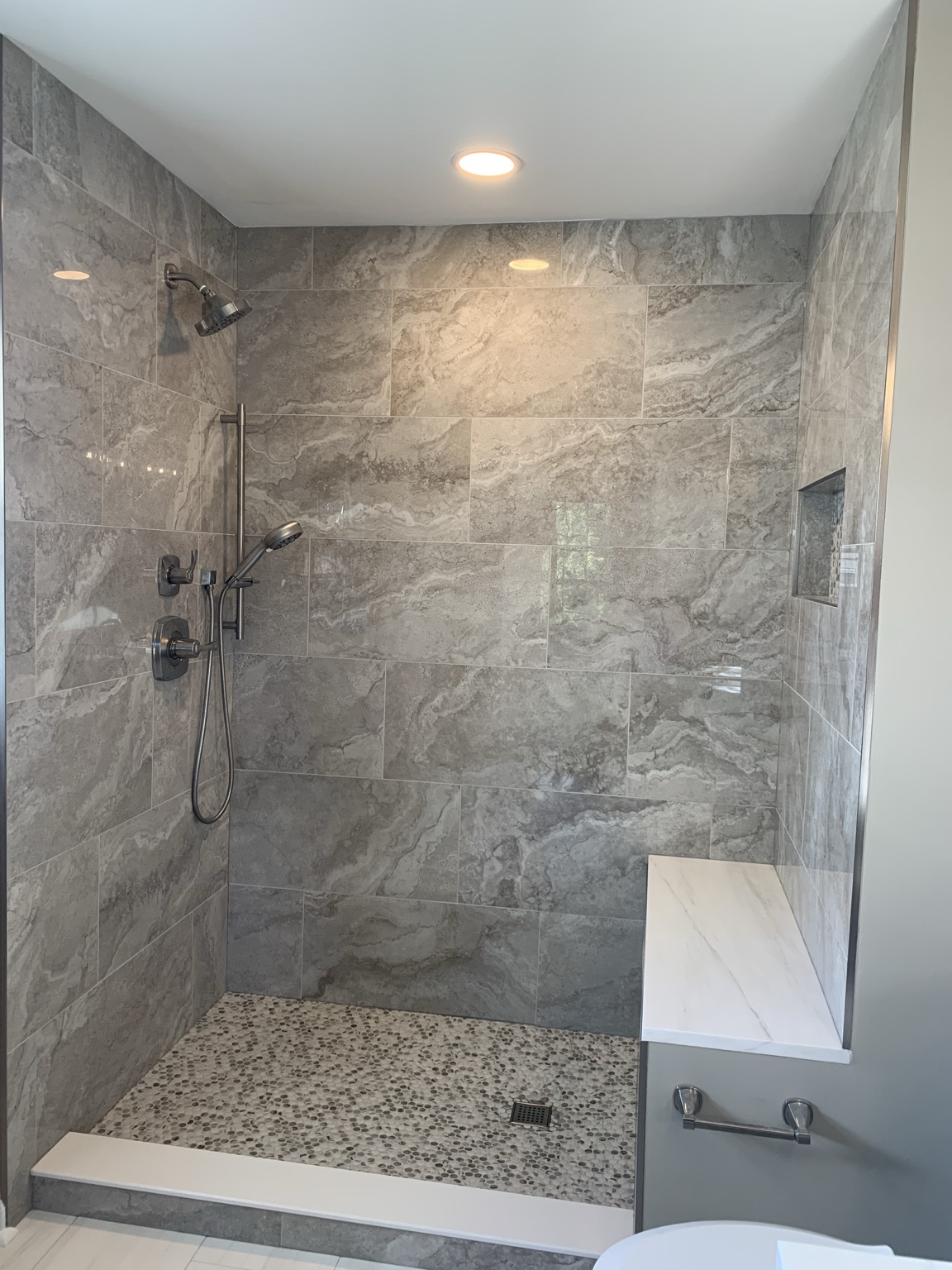 Large walk-in shower that replaced the original garden tub, with frameless glass, a marble bench, built-in niche, and penny tile floor.