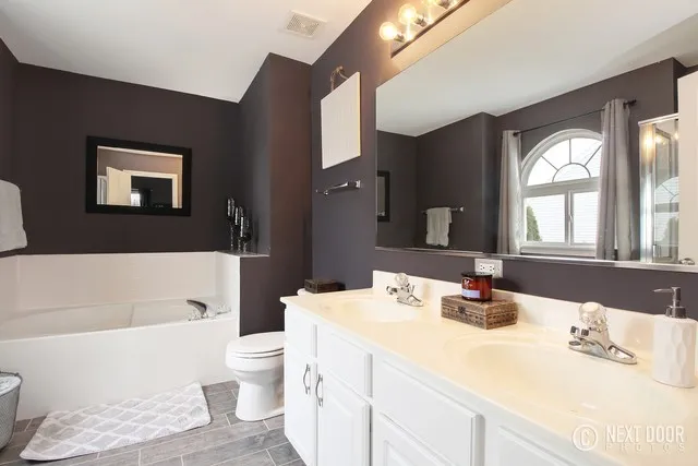 Master bathroom before the renovation with a garden tub, white double vanity, plum walls, and separate shower.