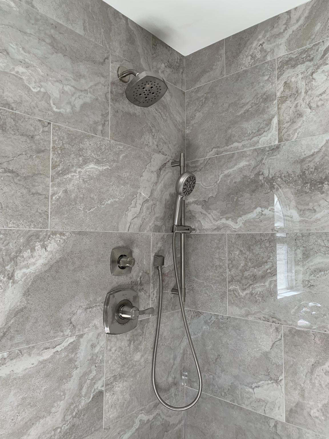 Delta Stryke shower fixtures against Novara Greige tile with soft, flowing gray and greige movement.