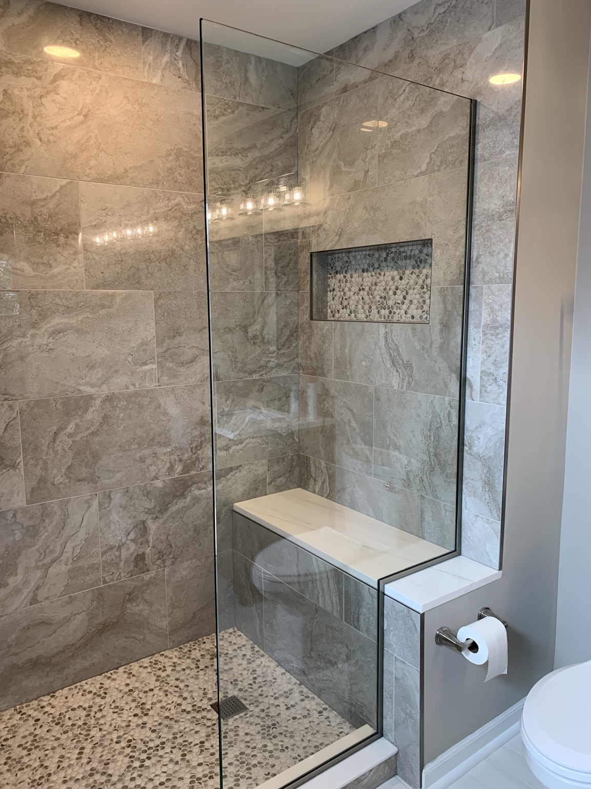 Walk-in shower with a polished marble bench, built-in niche, frameless glass, and penny mosaic floor.