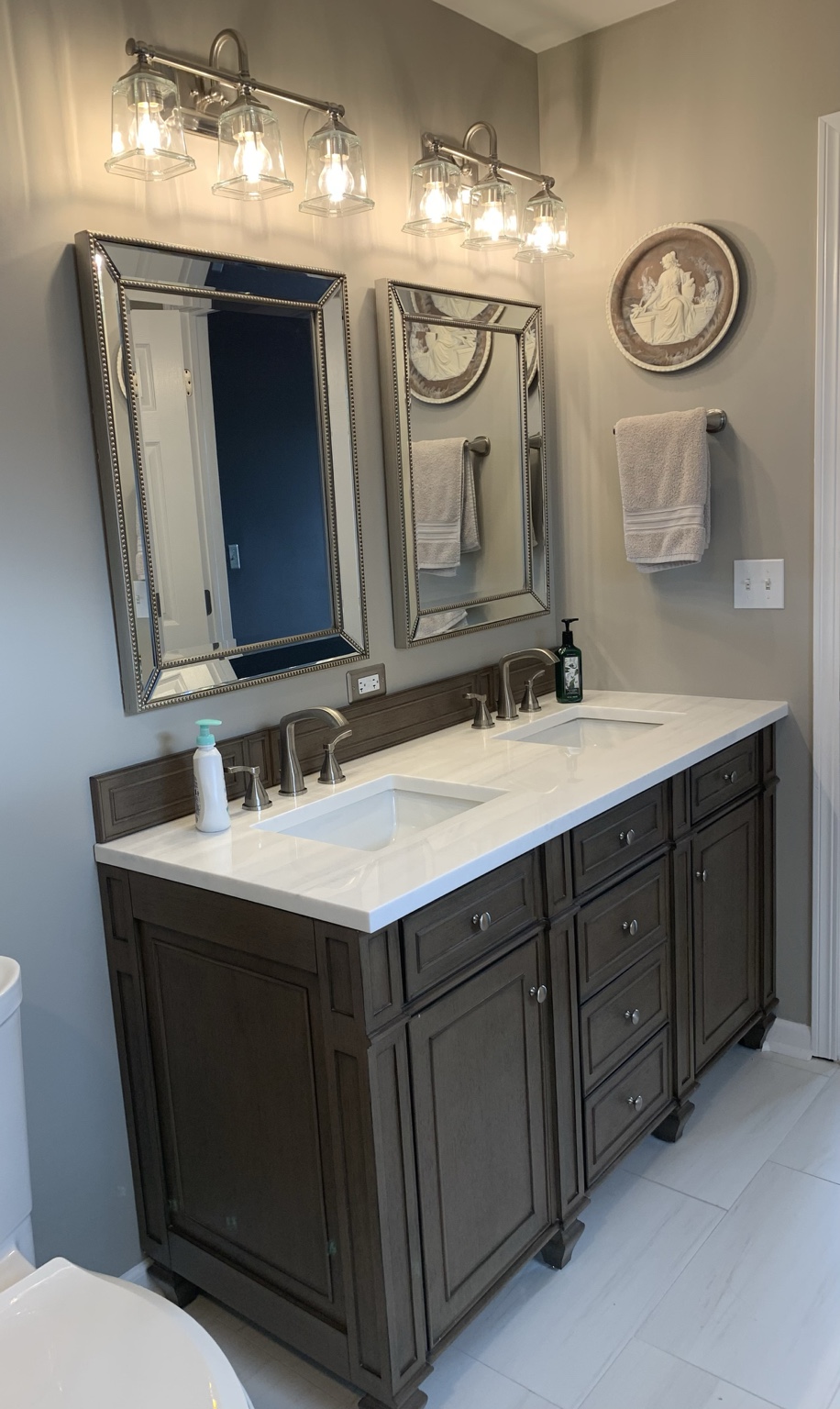 Whitewashed walnut vanity with a light striated countertop, stainless faucets, champagne-beaded mirrors, and brushed nickel lighting.